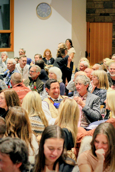 people gathered in a hall during the First Chair Gala. The image focus is on a man with dark hair, who is wearing O-A-S goggles around his neck, and grinning largely. 